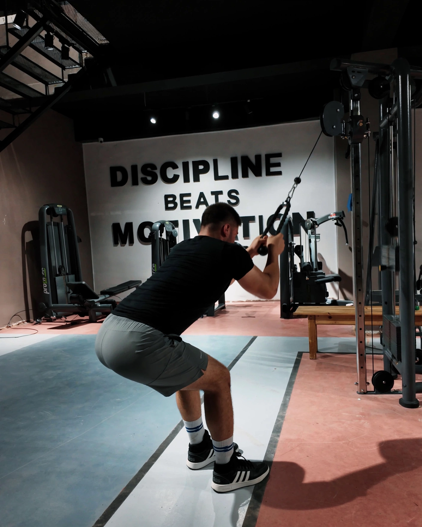 Arenium Fitness Center salonunda kablo makinesinde çalışan bir üye, arkasında duvara yazılmış DISCIPLINE BEATS MOTIVATION yazısı